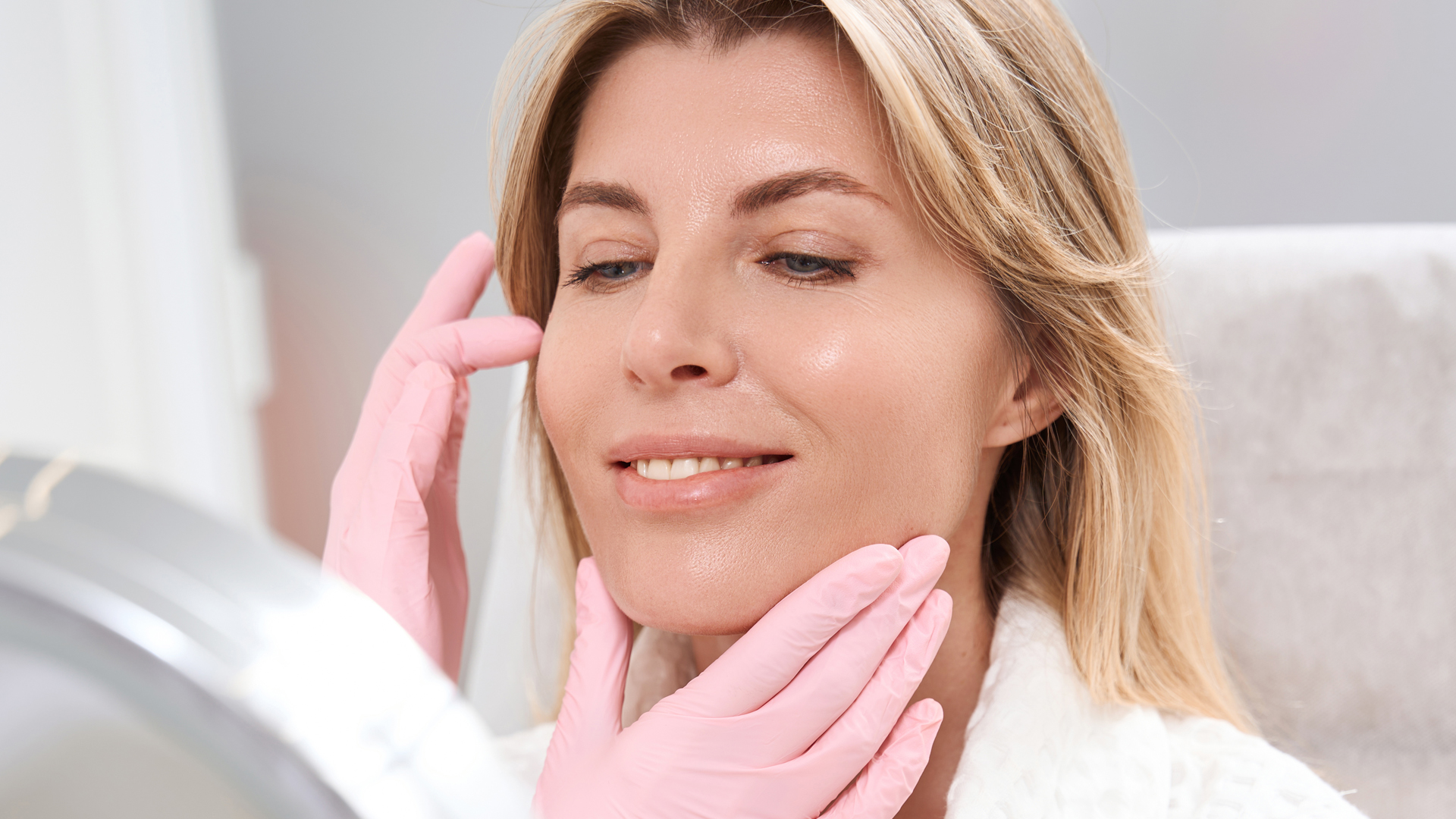 Woman drying face with pink towel after dental care or skincare routine indoors.