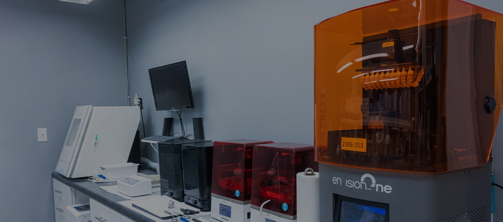 Modern dental office equipment including 3D printer and computer workstation in clinical setting.