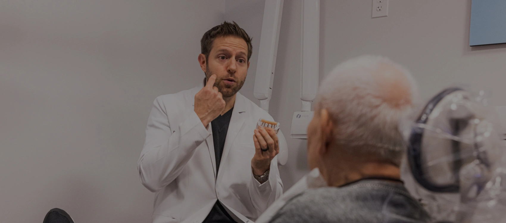 Dentist in white coat discussing treatment with senior male patient in dental office.