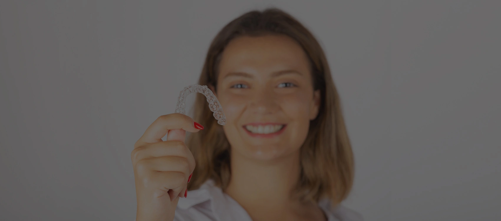 Woman giving thumbs up gesture against neutral background, smiling at camera