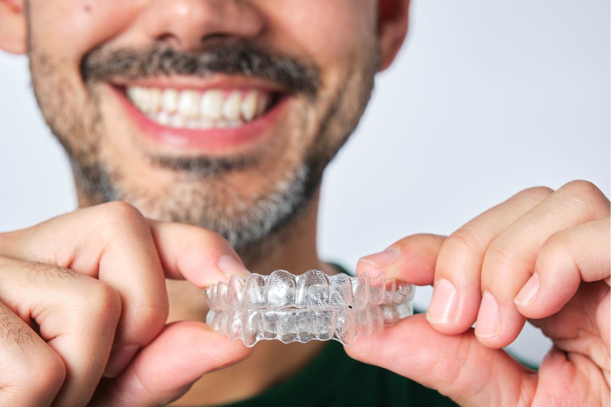 Smiling man holding clear aligner tray, demonstrating modern orthodontic treatment in dental office setting.