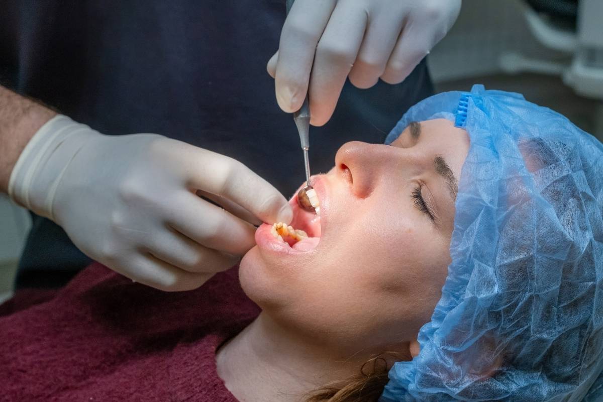 Dentist performing gum graft procedure on patient wearing blue protective head covering.