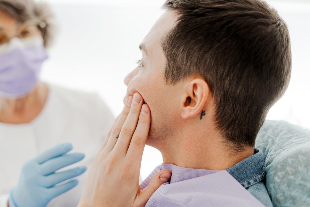 Man holding his cheek in pain during a dental consultation about untreated cavities.