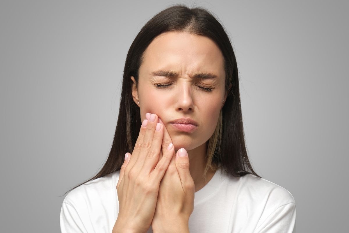 Woman with jaw pain holding her cheek, illustrating discomfort from chewing or biting issues.