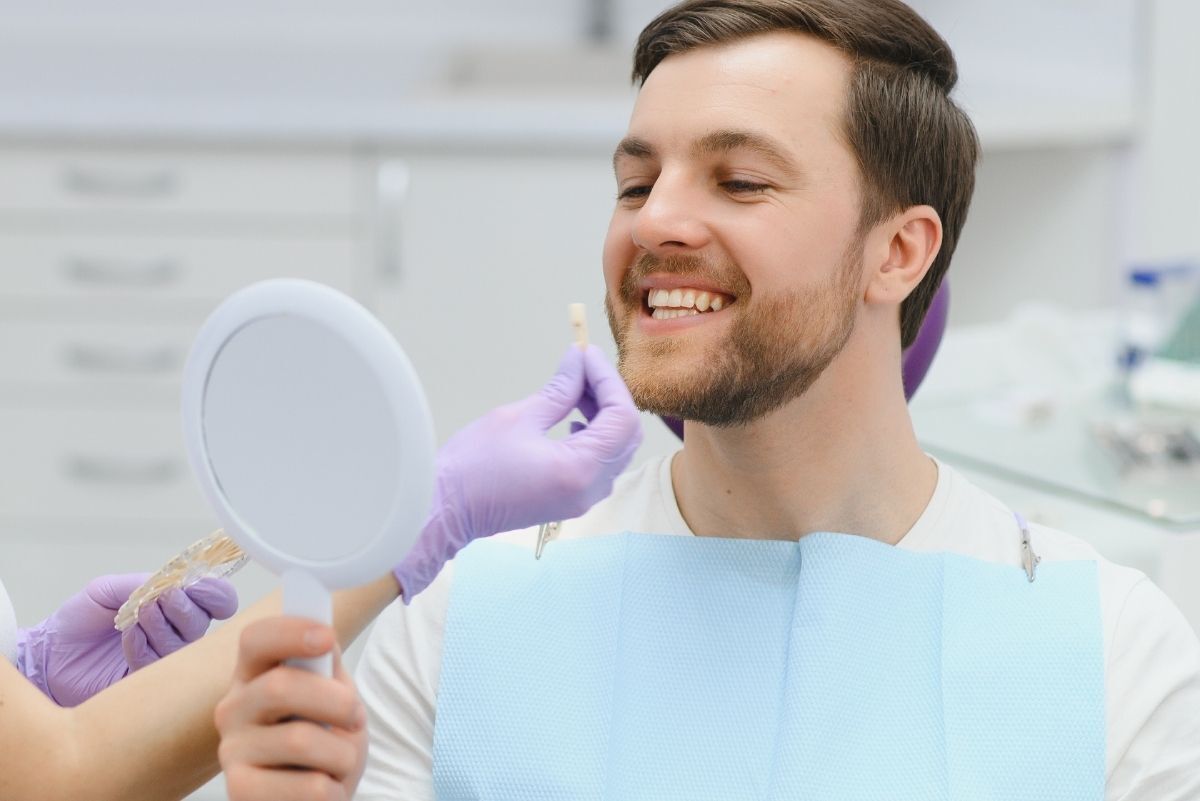 Happy male patient admiring his improved smile in mirror after cosmetic dental treatment in Knoxville.