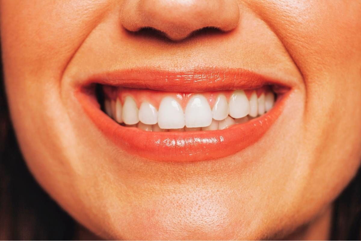 Close-up of a woman's bright white smile with coral lipstick and healthy teeth.