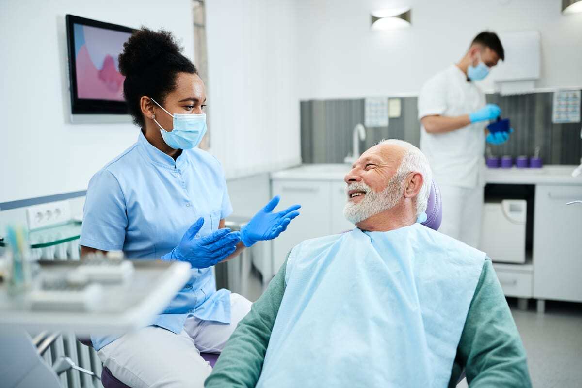 Smiling senior male patient consulting with female dentist about cavity prevention in dental office.